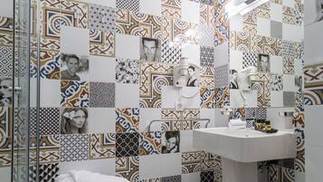 Casa de banho com azulejos estampados, lavatório e cabine de duche em vidro.