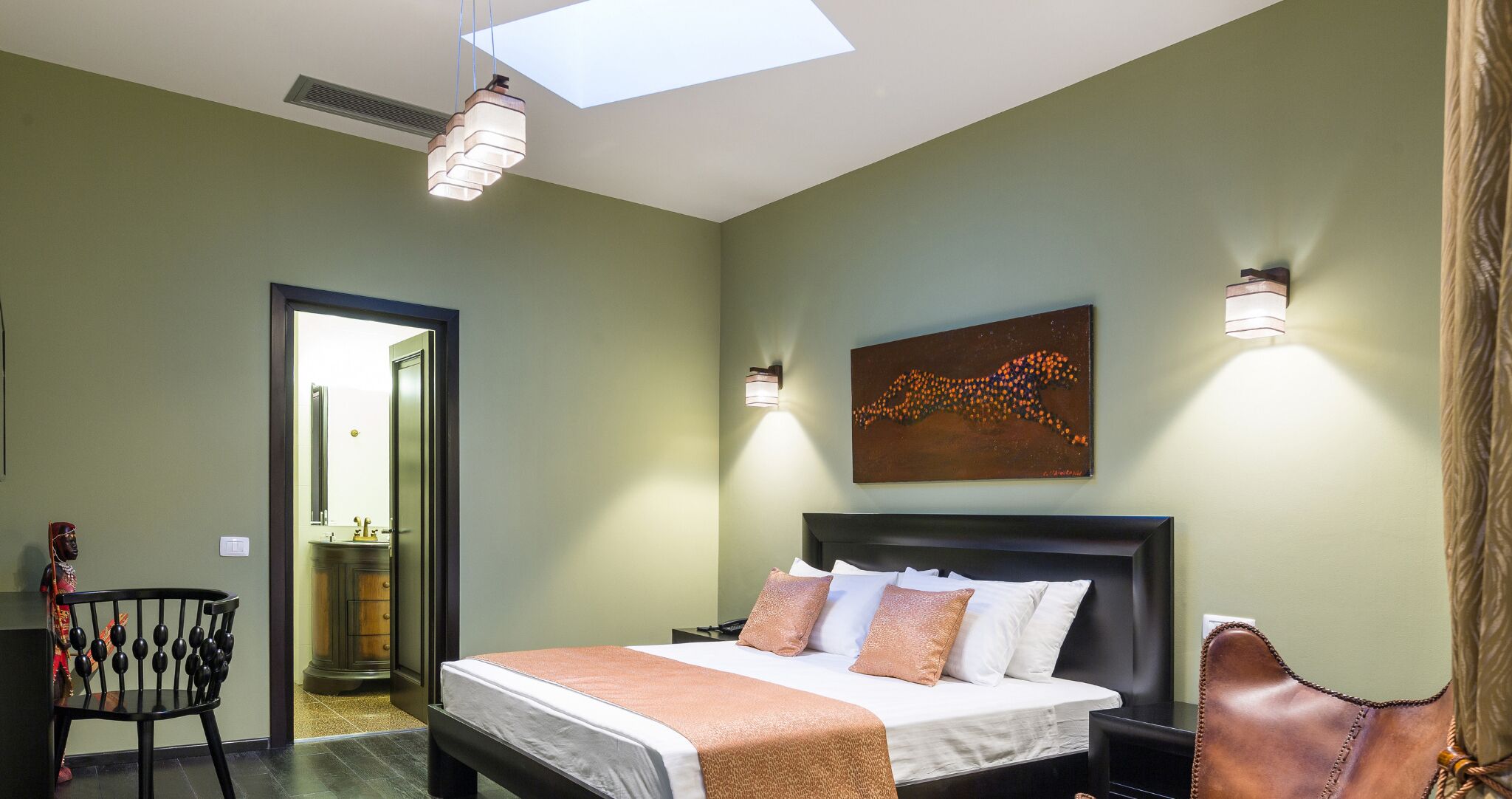 Un dormitorio con cama, mesita de noche, una silla, un cuadro y un tragaluz.