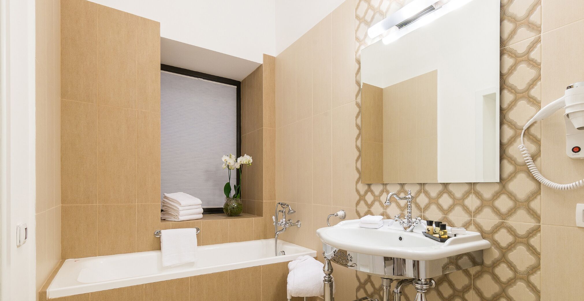 Un baño moderno con bañera, dos lavamanos, un espejo grande y un secador de pelo en la pared.