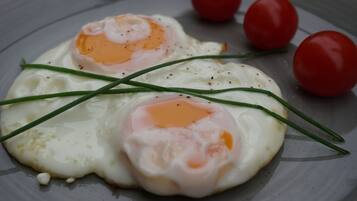 Two sunny-side-up eggs on a plate with cherry tomatoes and chives.