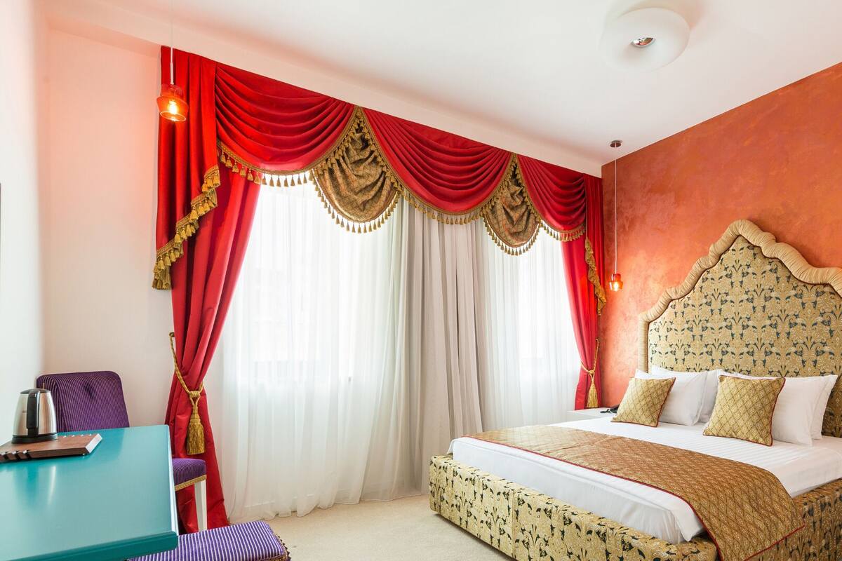A hotel room with a large bed, red curtains, and a patterned headboard.