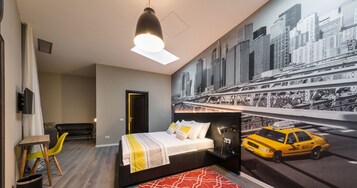 Habitación de hotel con cama, escritorio, silla, televisor y un mural con vista a la ciudad.