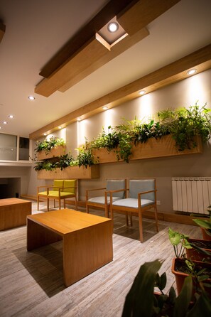 A modern interior with wooden beams, recessed lighting, and built-in planters with greenery. There are two wooden chairs and a table. - Hotel EcoSki by bund (San Carlos de Bariloche)