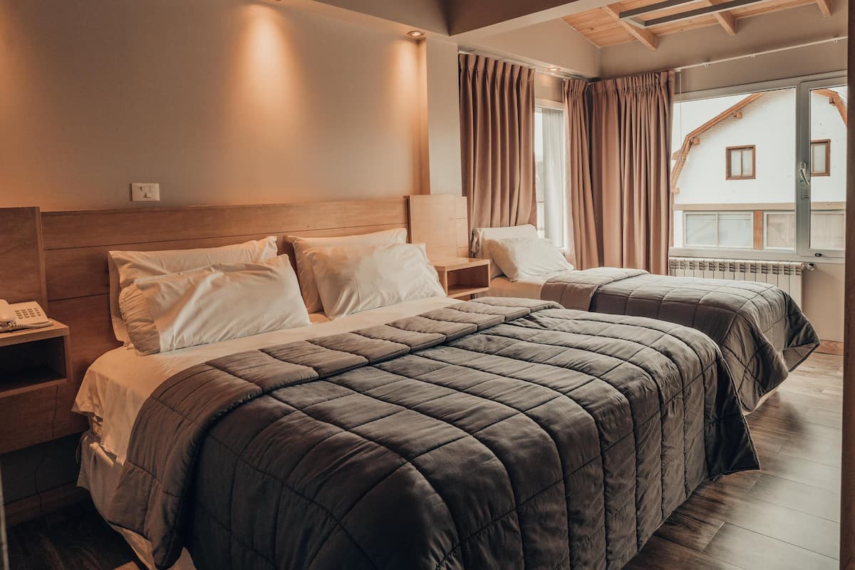 Une chambre d’hôtel avec deux lits, une table de chevet avec un téléphone et une fenêtre avec des rideaux.