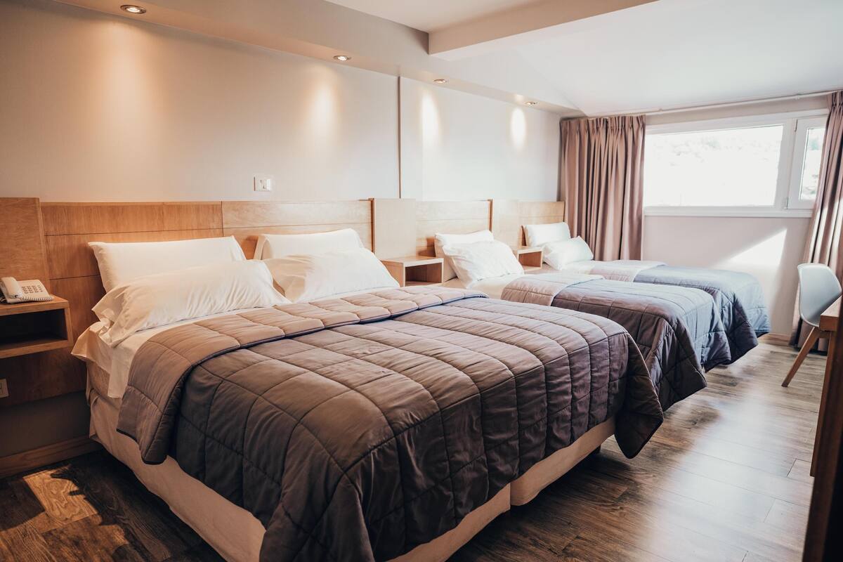Une chambre d’hôtel avec deux lits, des têtes de lit en bois, des tables de chevet avec des lampes, un téléphone sur la table de gauche et une fenêtre avec des rideaux.