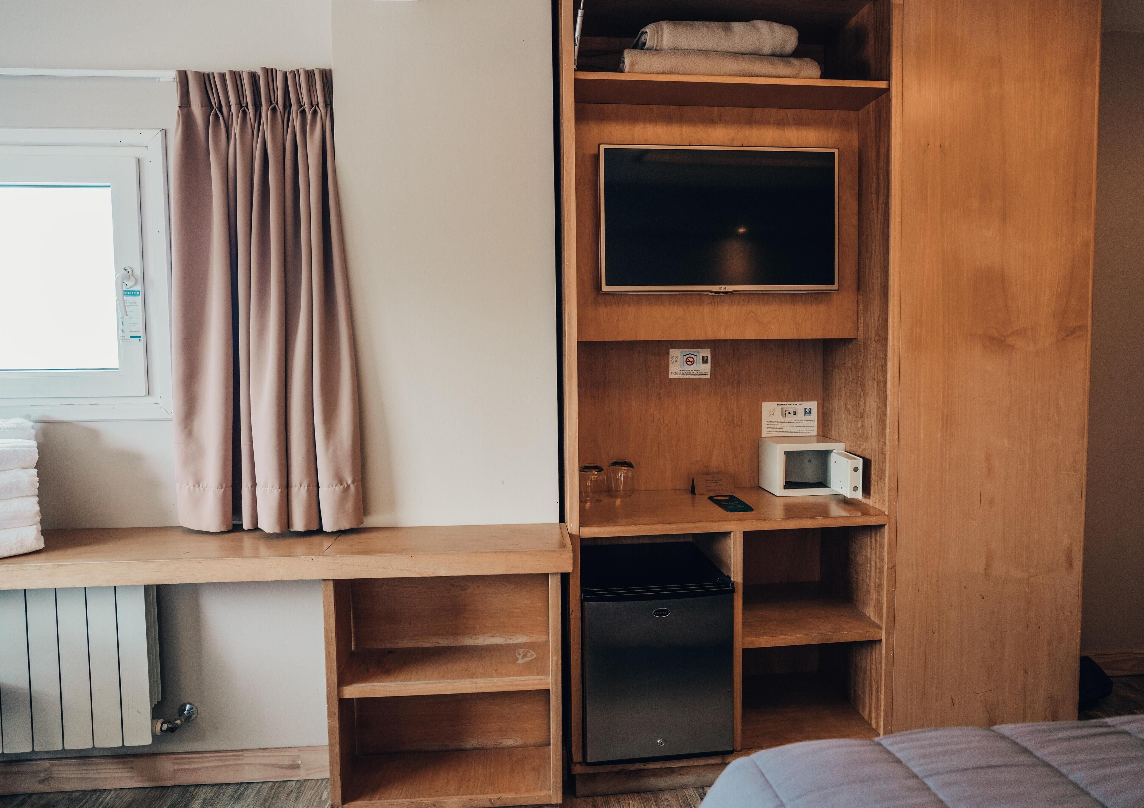 A compact room with a wooden desk, a television, a microwave, and a small refrigerator.