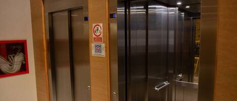 A modern elevator with metallic doors and a wooden panel wall.