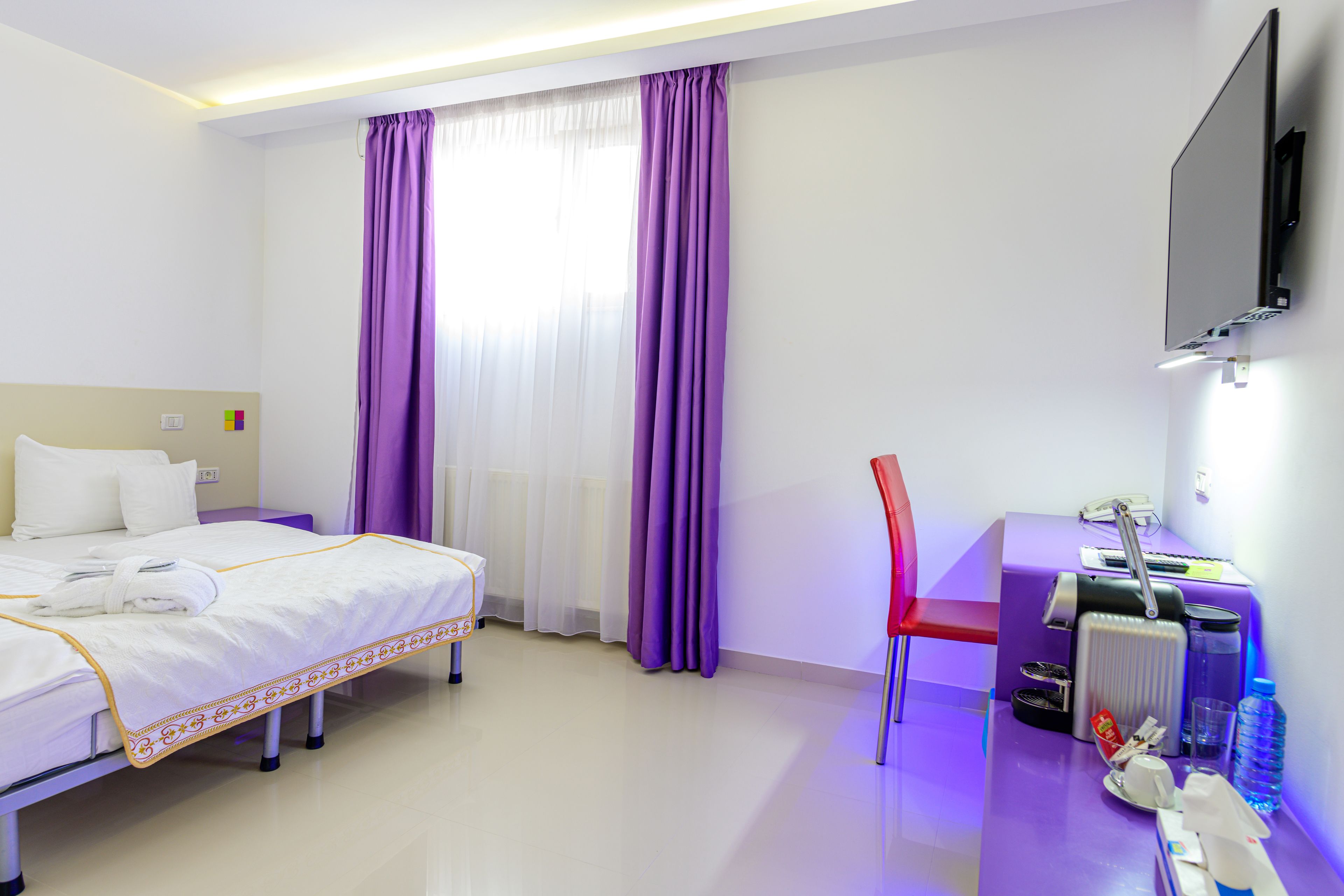 Una habitación de hotel con una cama, un escritorio con computadora, una silla y un televisor montado en la pared.