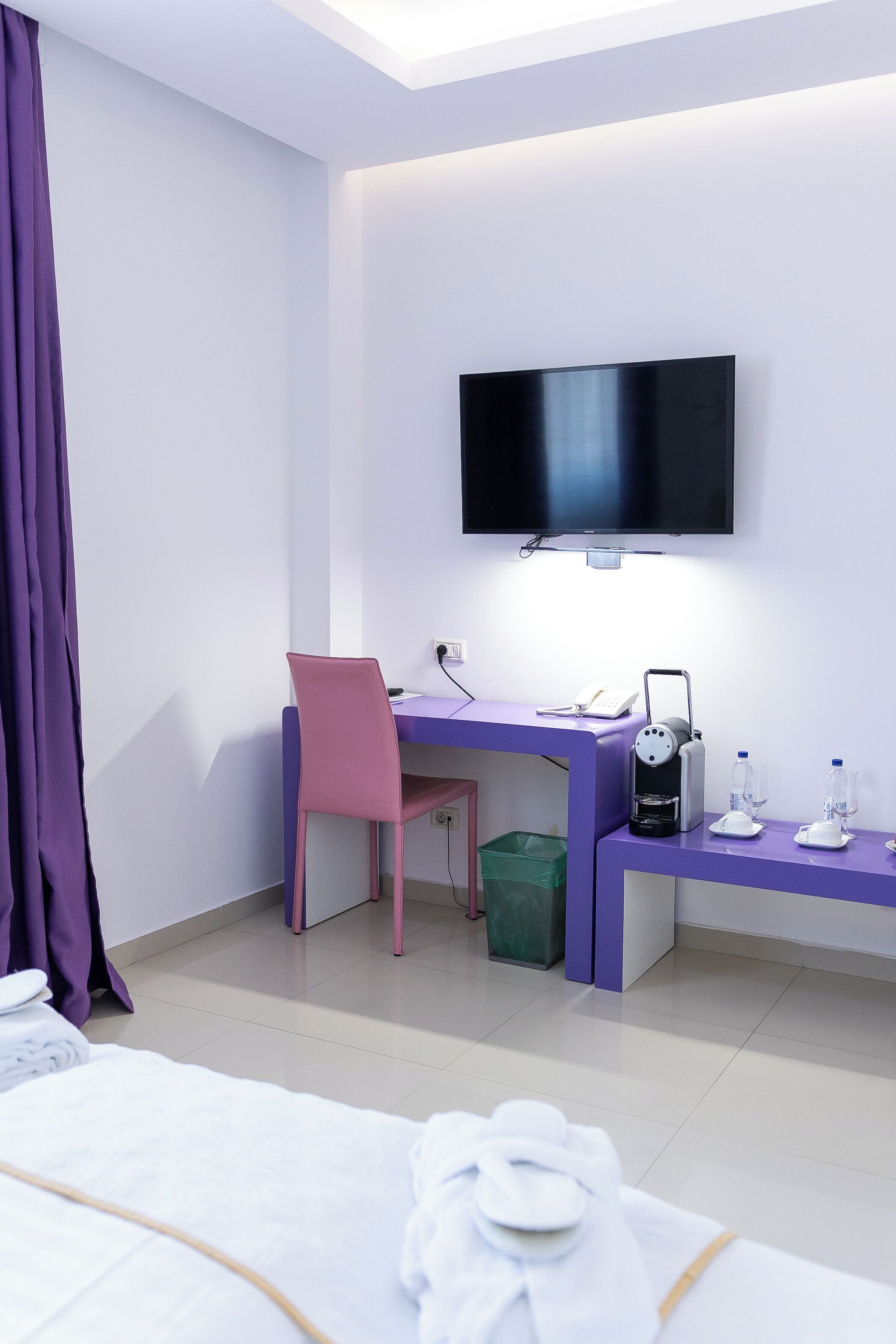Une chambre d’hôtel comprenant un lit, un bureau avec une chaise, une télévision, une machine à café et une poubelle.