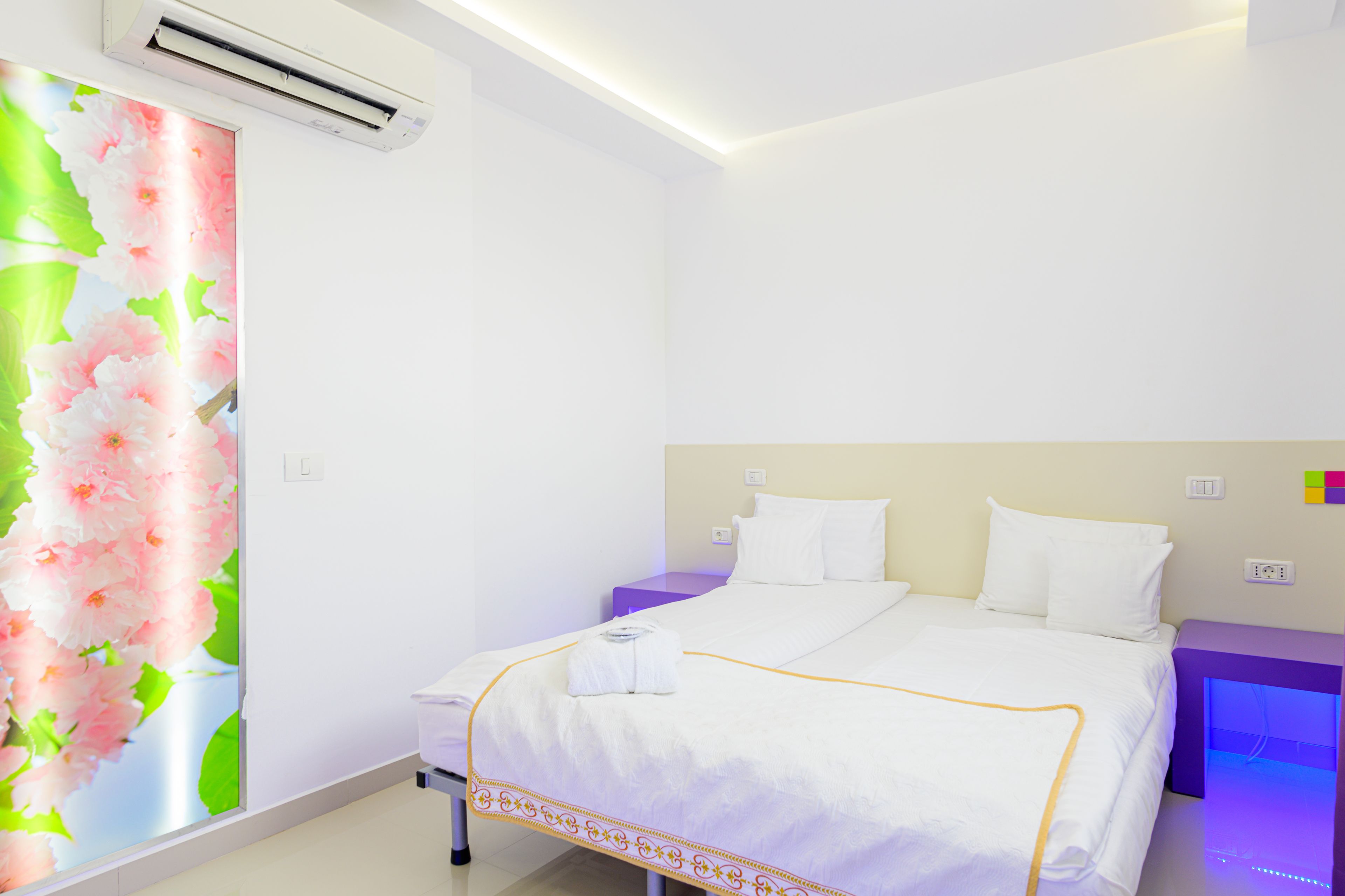 A modern hotel room with a large bed, a bedside table, an air conditioner, and a wall with a floral wallpaper.