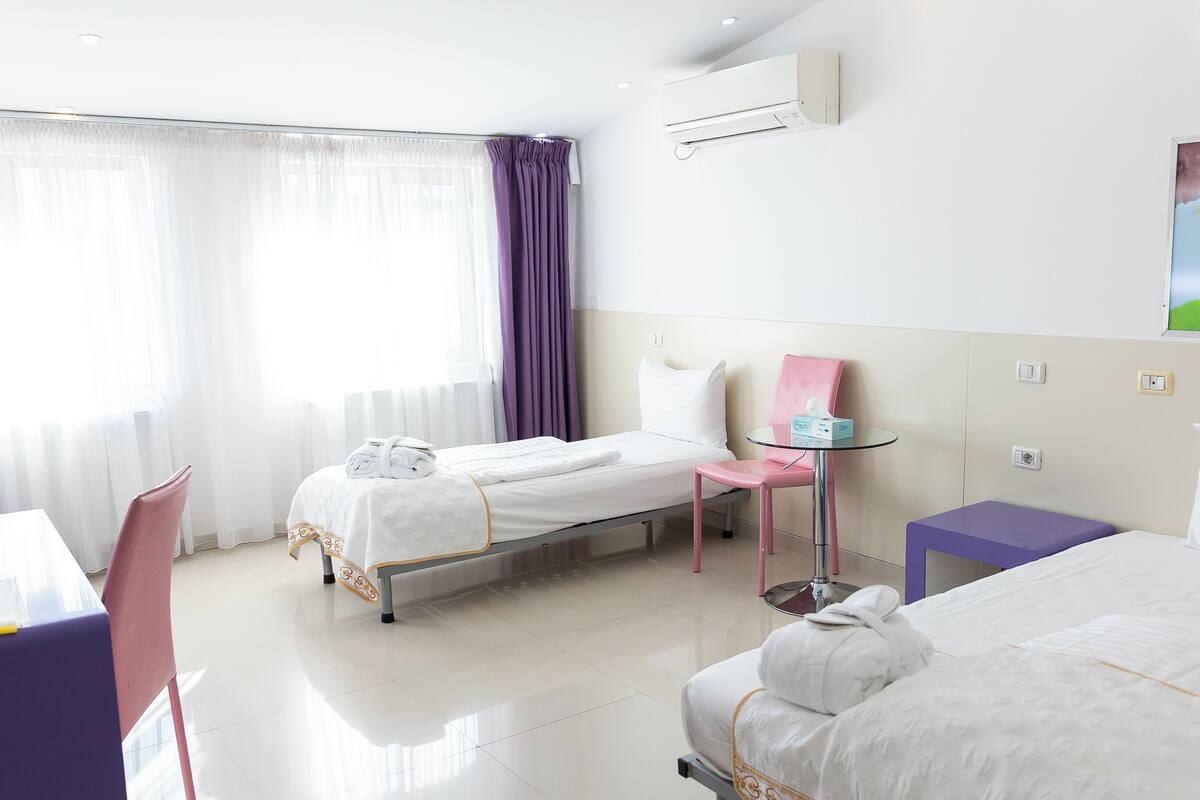 Une chambre d’hôtel avec un lit, une chaise, une petite table et une fenêtre avec des rideaux.