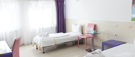 A hotel room with a bed, a chair, a small table, and a window with curtains.