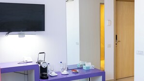 Ein modernes Hotelzimmer mit einem violetten Schreibtisch, einem großen Spiegel, einem Flachbildfernseher und einer Holztür.