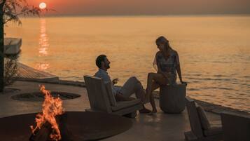 A couple sitting by a fire pit at sunset with a view of the ocean.