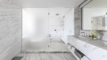 Ein modernes Badezimmer mit Marmorboden, einer Glasdusche, einem großen Spiegel und einer Marmorplatte mit Blumen.