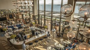 Un hall de hotel espacioso con zona de bar, arreglos de asientos y ventanas grandes que ofrecen vista al mar.