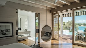 Un dormitorio moderno con una silla colgante, un ventanal grande y vistas a una piscina y paisaje.