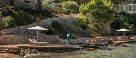 A coastal resort with a stone wall, lounge chairs, and umbrellas by the water.