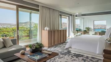 Une chambre d’hôtel moderne avec un grand lit, un canapé, une table basse avec un livre et une plante, et une vue sur le paysage.