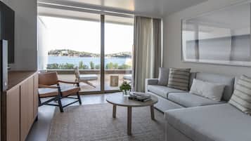 Un salón moderno con sofá, mesa de centro y televisor. Se ve el mar a través de amplias ventanas.