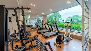 A gym with cardio machines, weight training equipment, and a large window with a view of greenery. - Langhetto Siena (Gramado)