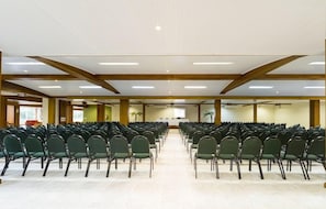 A large conference room with rows of green chairs, wooden beams on the ceiling, and a projector screen at the front. - Langhetto Siena (Gramado)
