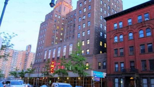 Un immeuble à plusieurs étages, reconnaissable à son grand panneau « YMCA » sur la façade, entouré d’autres bâtiments.