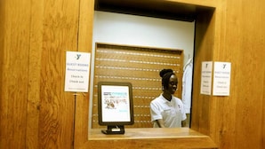 Un comptoir d’accueil avec un écran d’ordinateur affichant une carte, le tout entouré de panneaux de bois. On y trouve des panneaux indiquant les informations relatives aux réservations et aux départs des chambres.