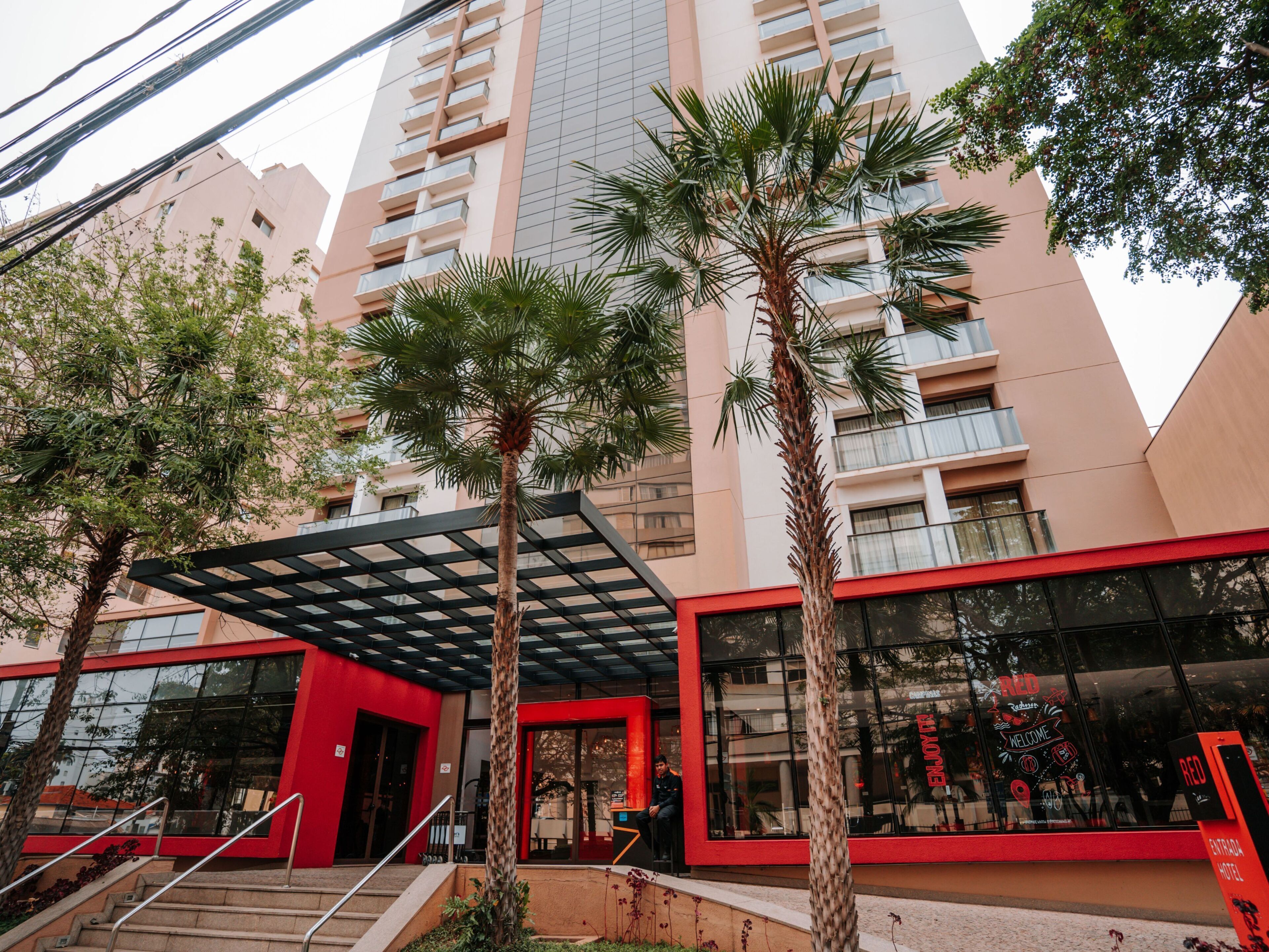 A modern building with a red facade, large windows, and a covered entrance area.