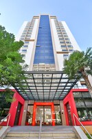 Un edificio moderno con fachada de vidrio, entrada roja y una escalera que lleva a la entrada.