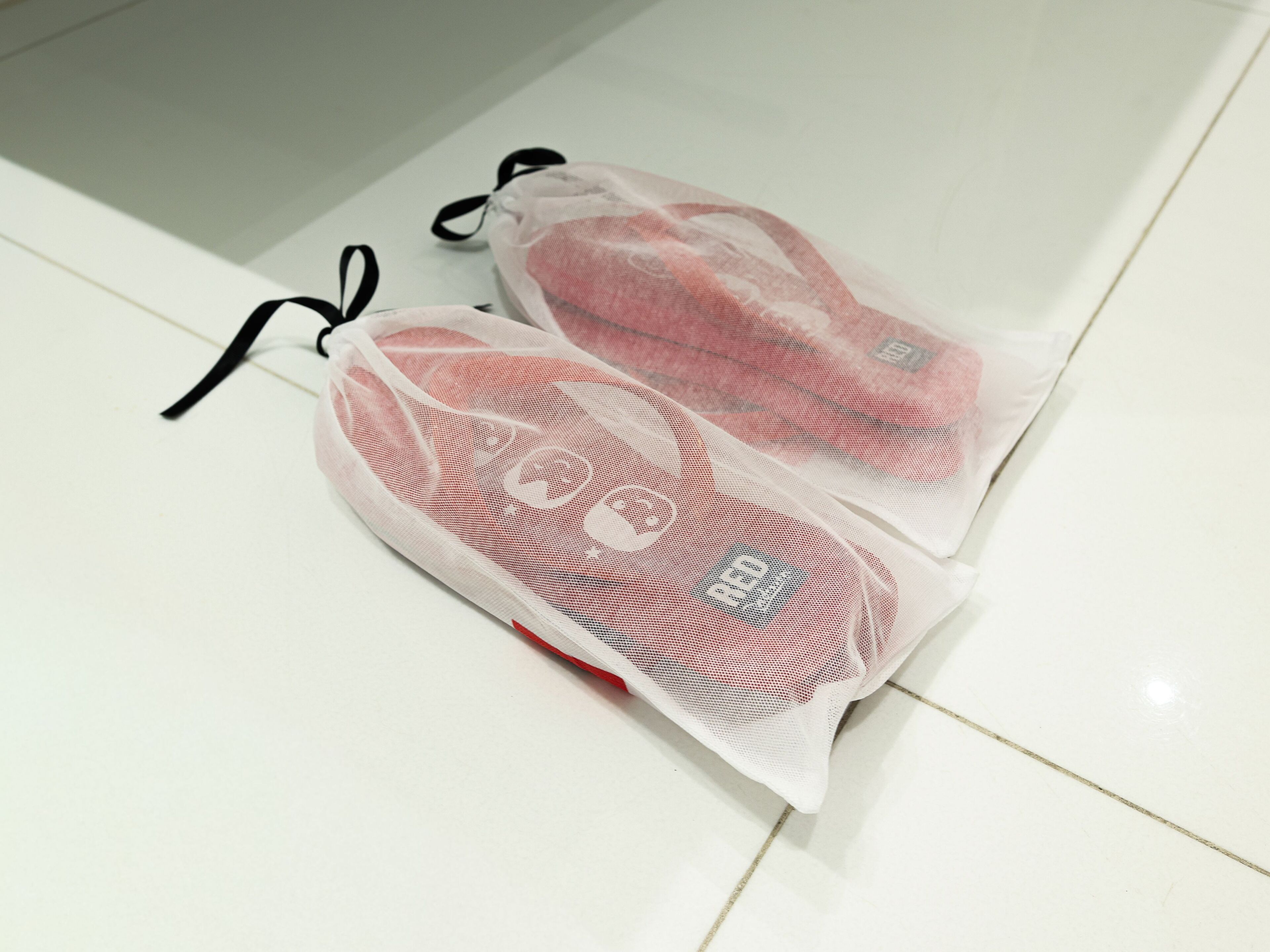 Duas sacas de malha com cordão em um chão de azulejos brancos.