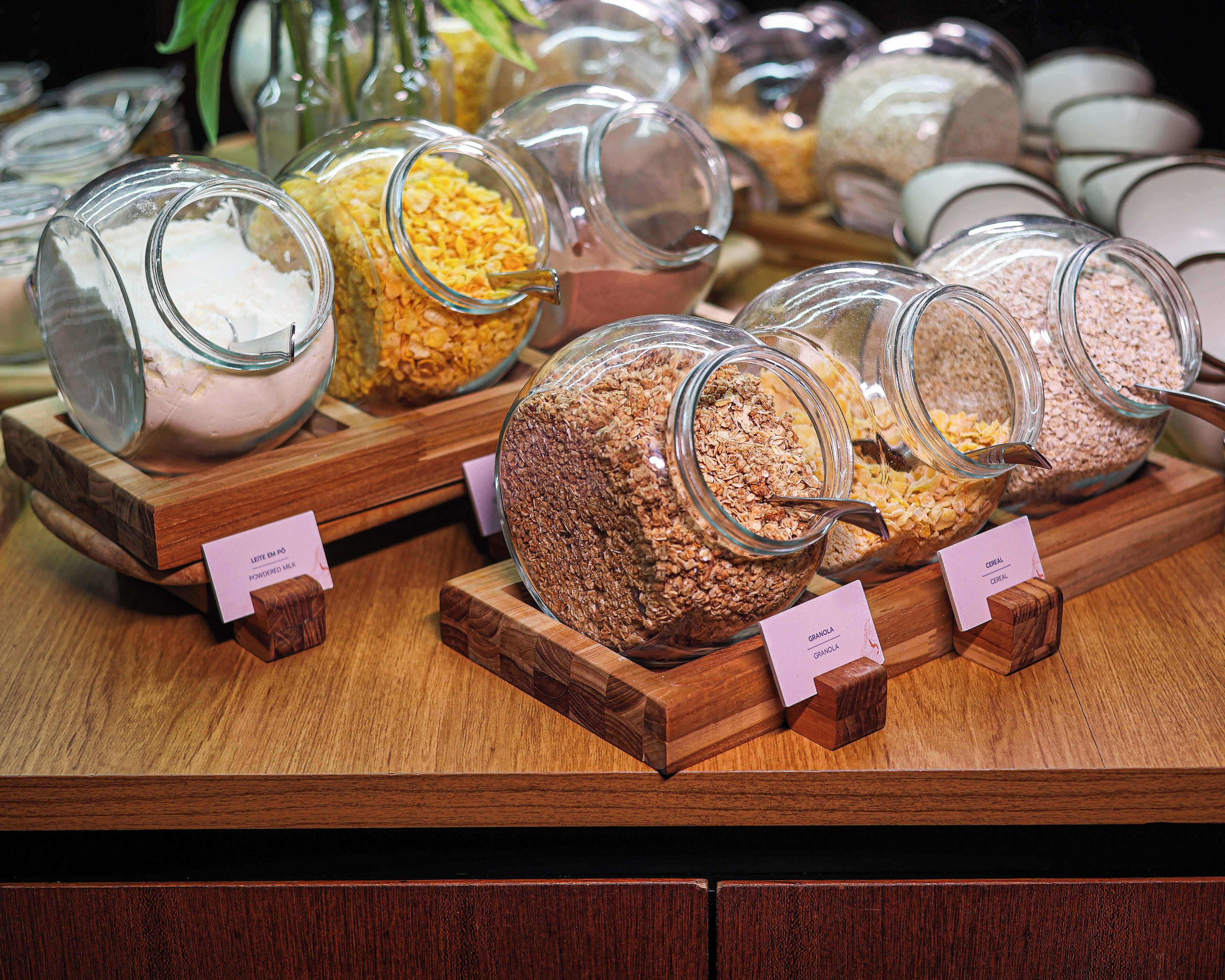 Una exhibición de diversos alimentos en recipientes de vidrio con etiquetas, dispuesta sobre pedestales de madera.