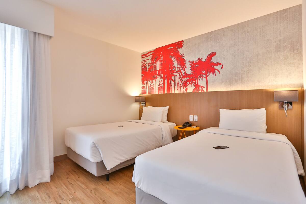 A hotel room with two beds, a wooden headboard, a wall-mounted phone, and a small table with a lamp.
