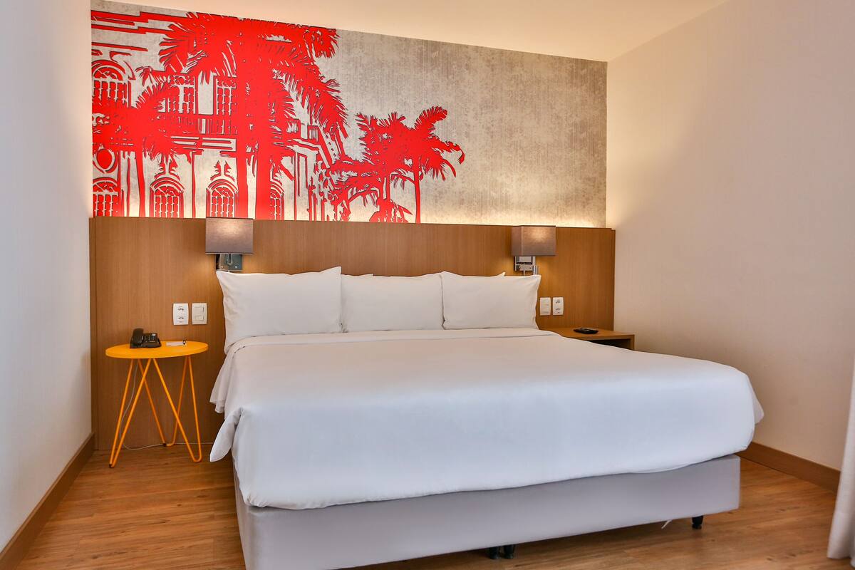 A hotel room with a large bed, two bedside tables, a wall-mounted artwork, and a wooden headboard.