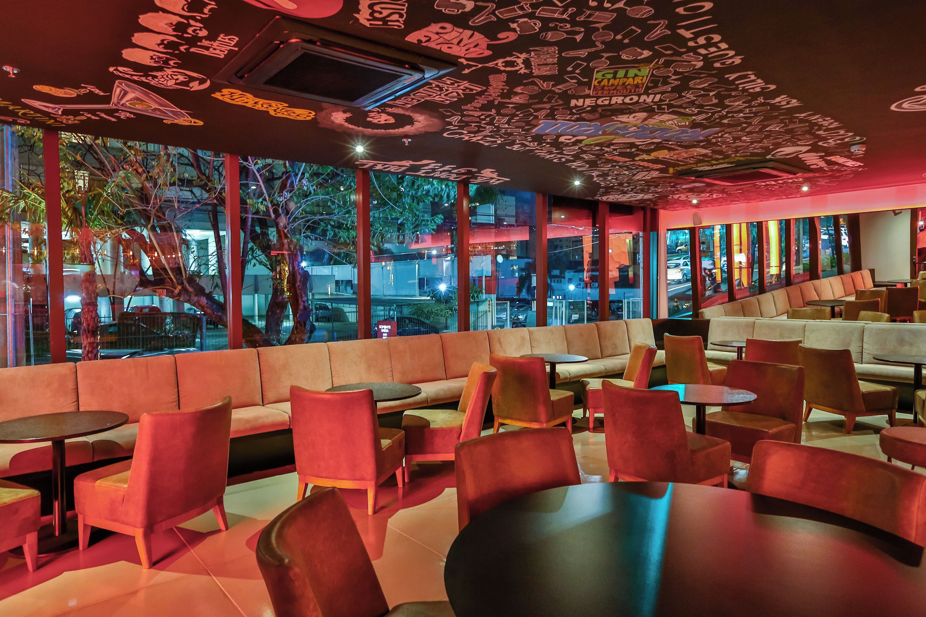 En modern restaurang med röda och beige möbler, stora fönster och ett tak som är dekorerat med olika typer av klotter och text.