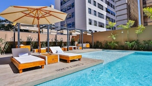 A poolside area with wooden loungers and a large umbrella. - Radisson RED Campinas (Campinas)