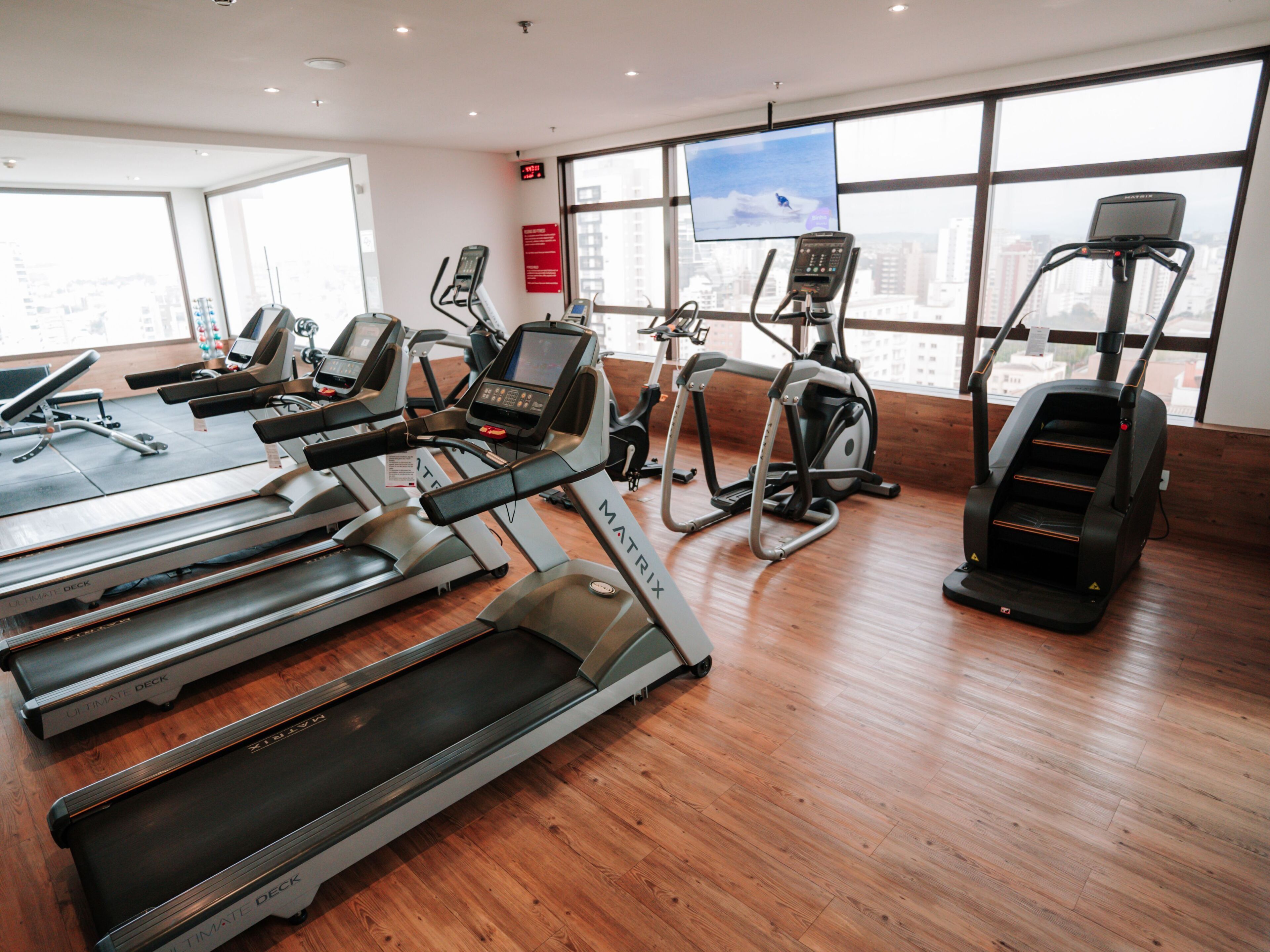 A gym with treadmills, elliptical machines, and a TV screen.