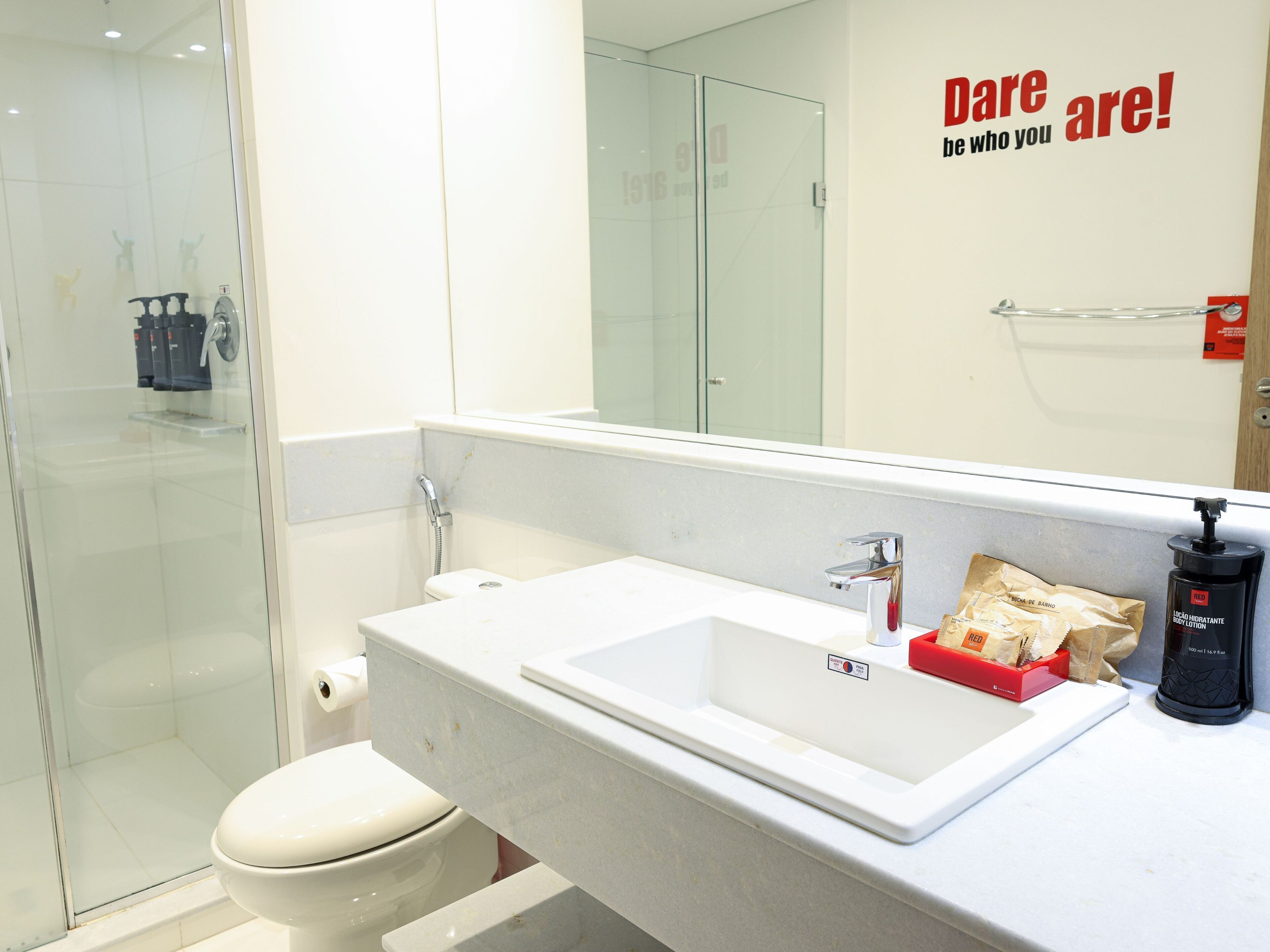 Baño con cabina de ducha de vidrio, lavabo blanco con espejo y artículos de aseo.