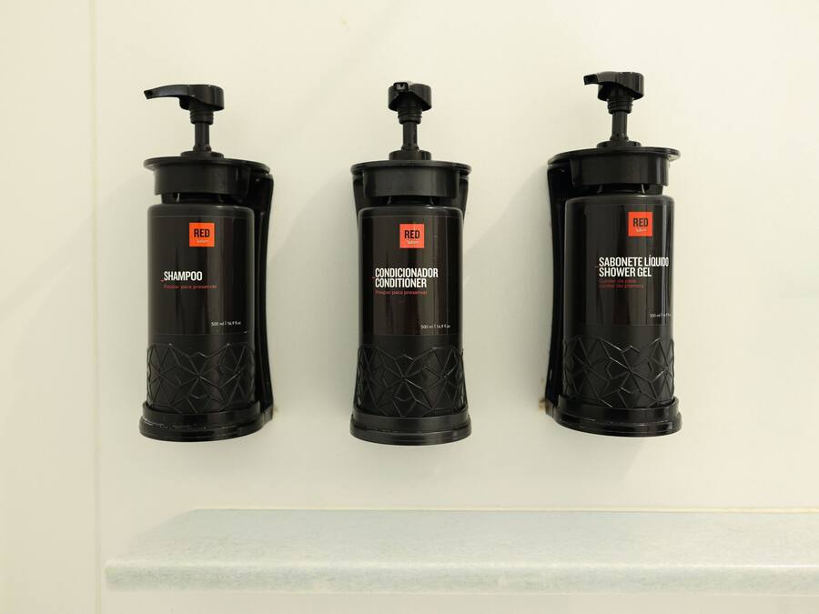 Three black bottles of Red shampoo, conditioner, and shower gel on a white wall.