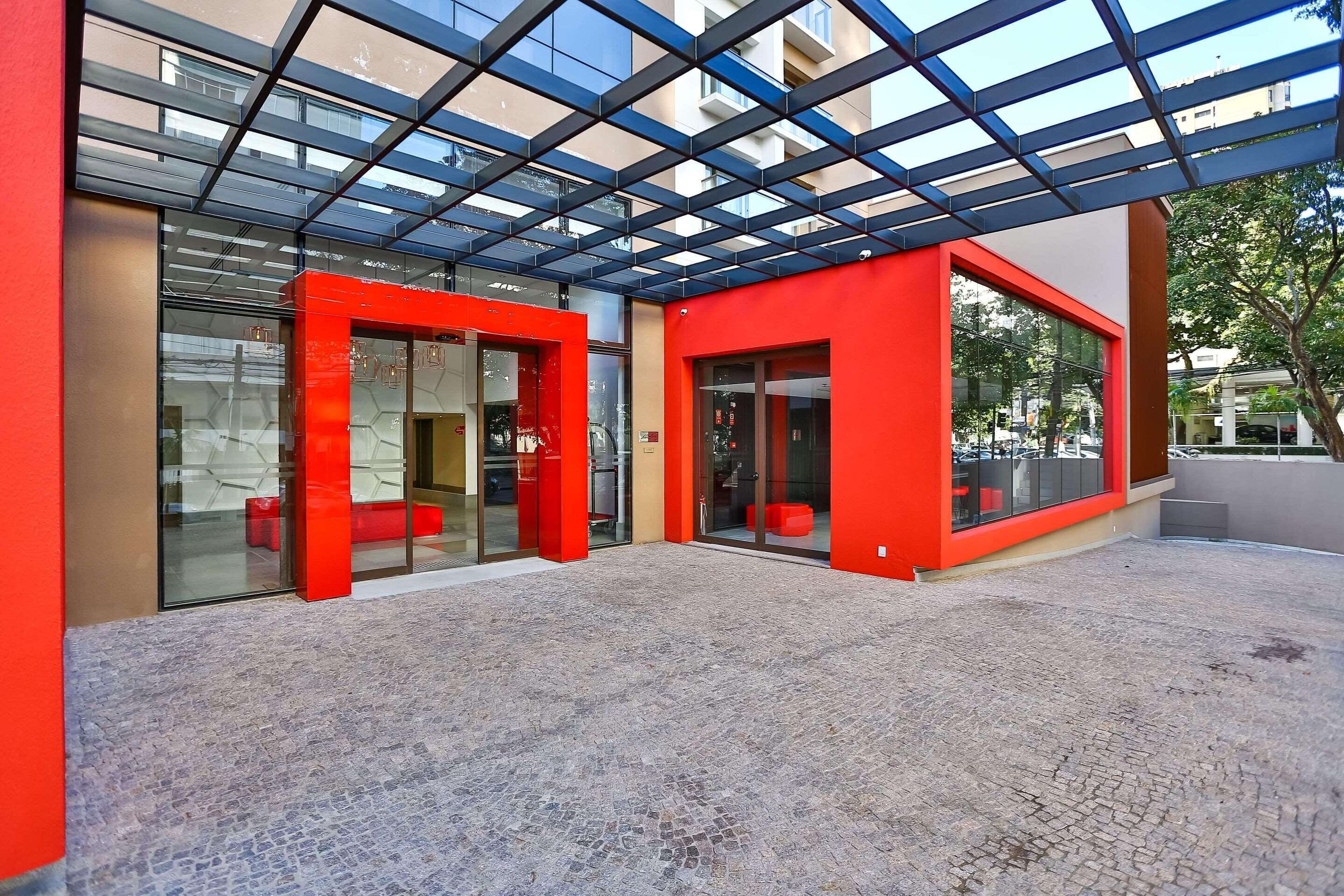 A modern building with a red facade, large glass windows, and a covered outdoor area with a patterned floor.