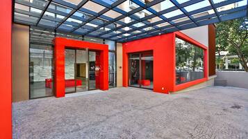 A modern building with a red facade, large glass windows, and a covered outdoor area with a patterned floor.