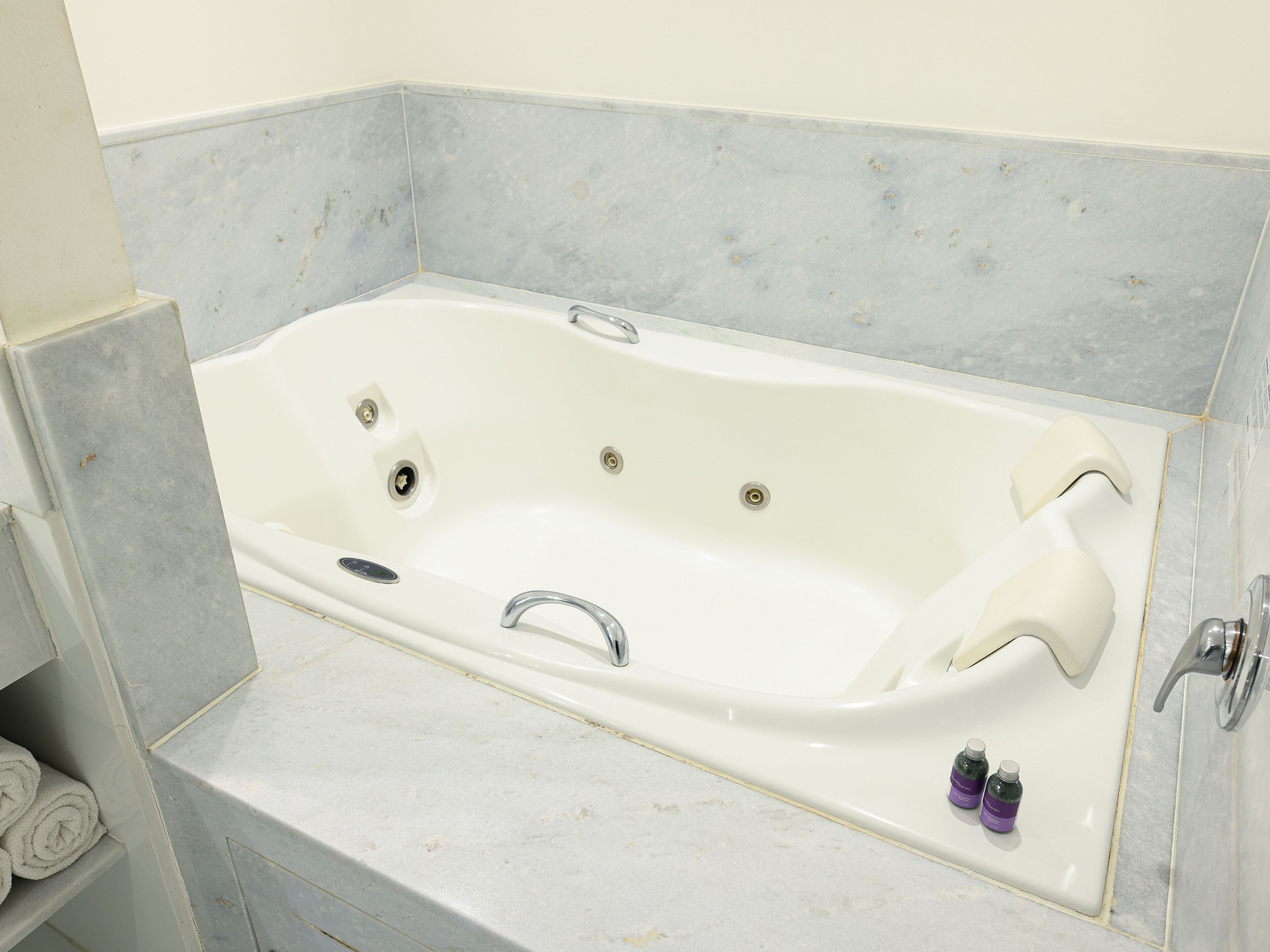A white bathtub with a single faucet, a built-in seat, and a small shelf with rolled towels.