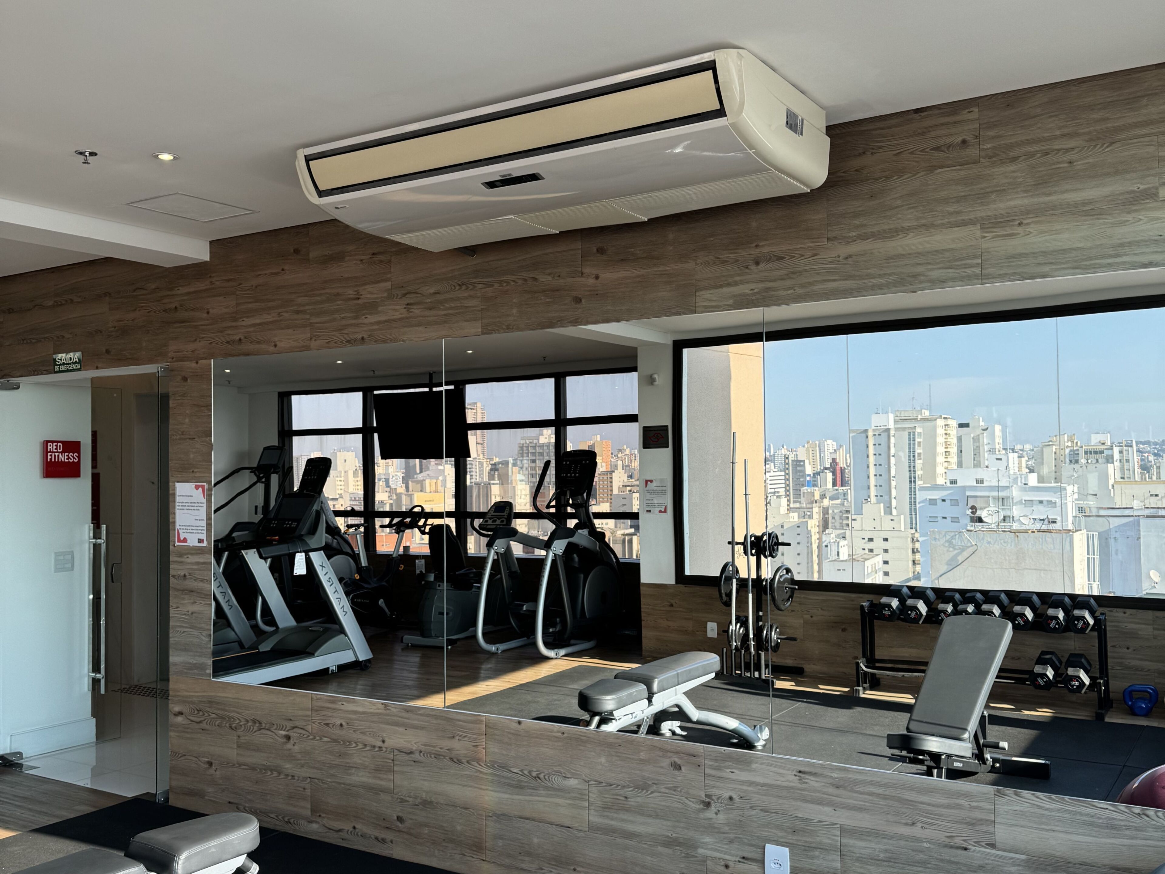 A gym with exercise equipment, a large mirror, and a city view through large windows.