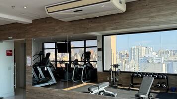 A gym with exercise equipment, a large mirror, and a city view through large windows.