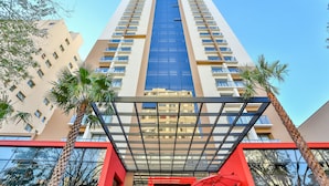 A high-rise hotel with a central glass elevator shaft, multiple balconies, and palm trees in the foreground. - Radisson RED Campinas (Campinas)