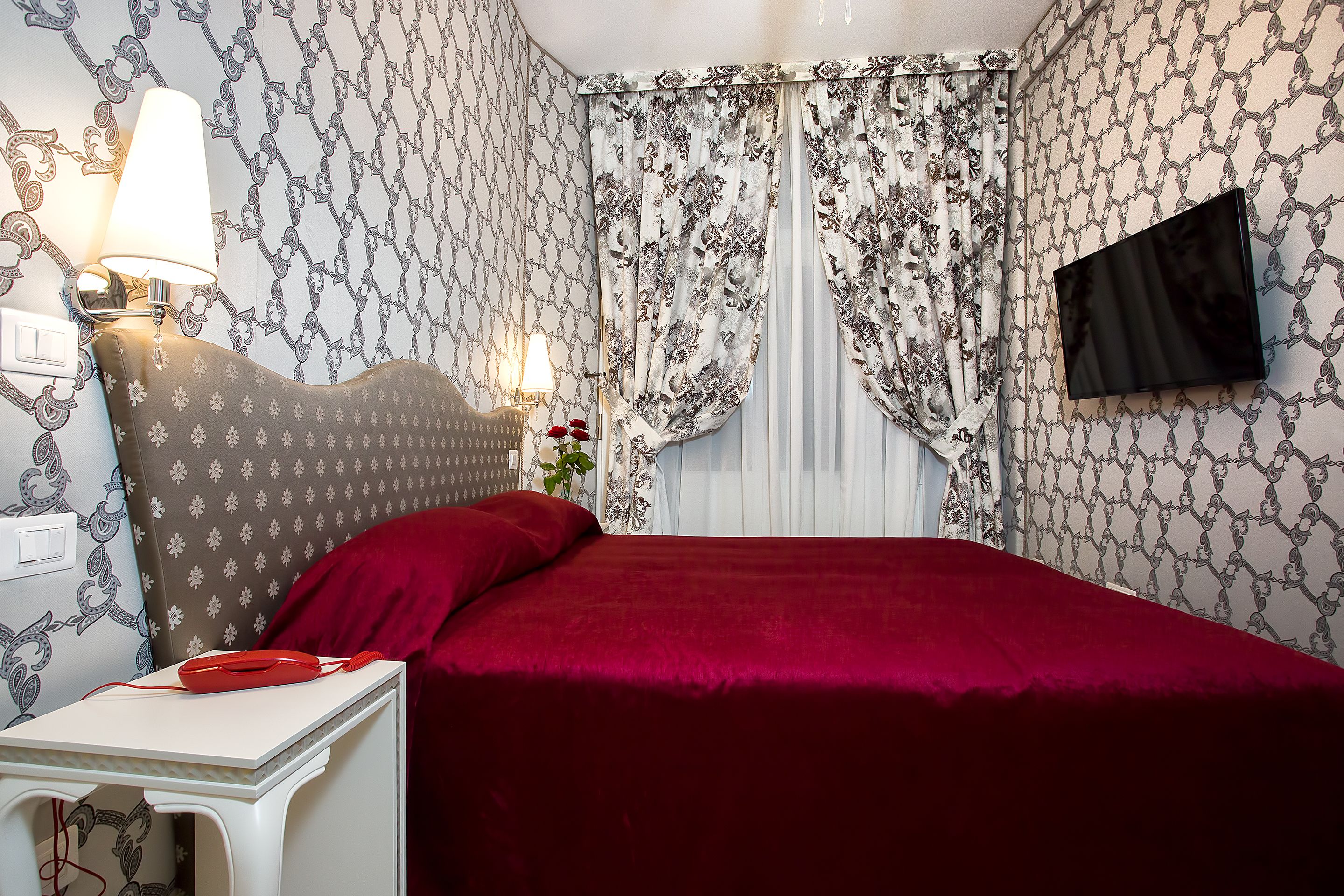 A neatly arranged bedroom with a bed, a bedside table, a lamp, and a TV mounted on the wall.