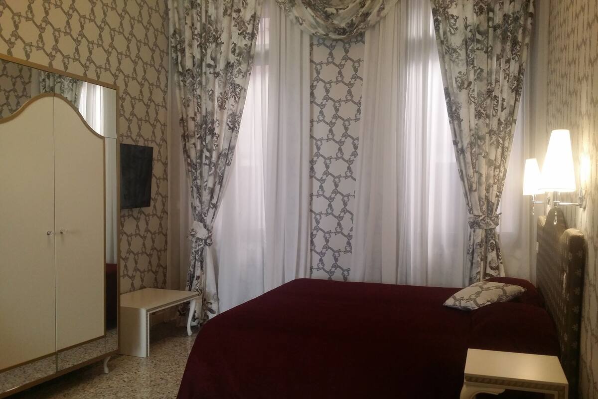 Un dormitorio con cama, mesita de noche, lámpara, armario y cortinas.