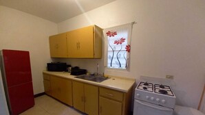 A compact kitchen with yellow cabinets, a red refrigerator, a gas stove, and a sink. - La Casa de Joy Airport Apartments (St. John's)