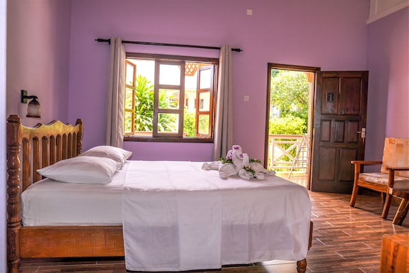 Un dormitorio con cama, cabecera de madera, ventana con cortinas, puerta y una silla.