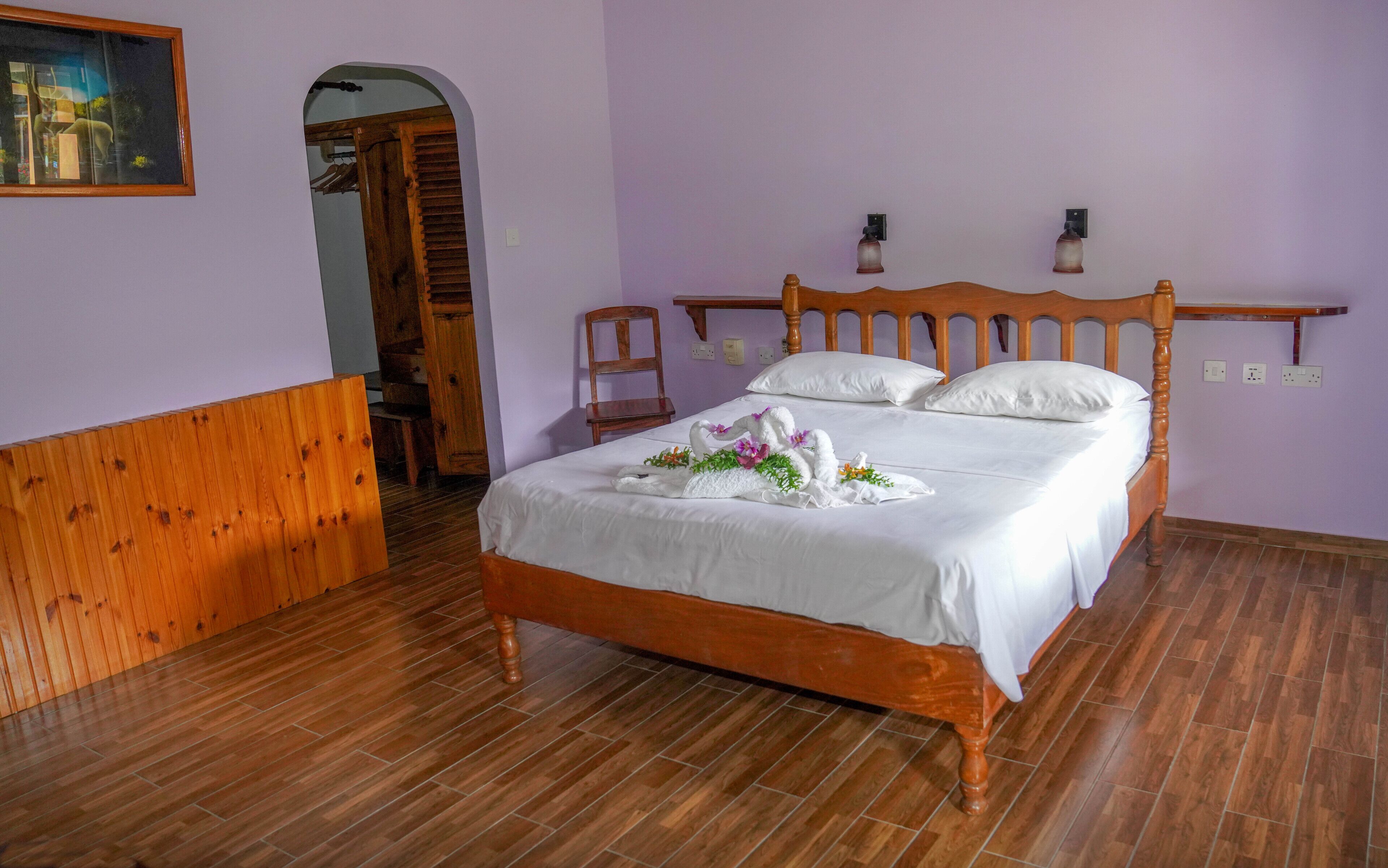 Ein ordentlich bezogenes Bett mit einem Holzkopfende, Holzboden und einer violetten Wand.